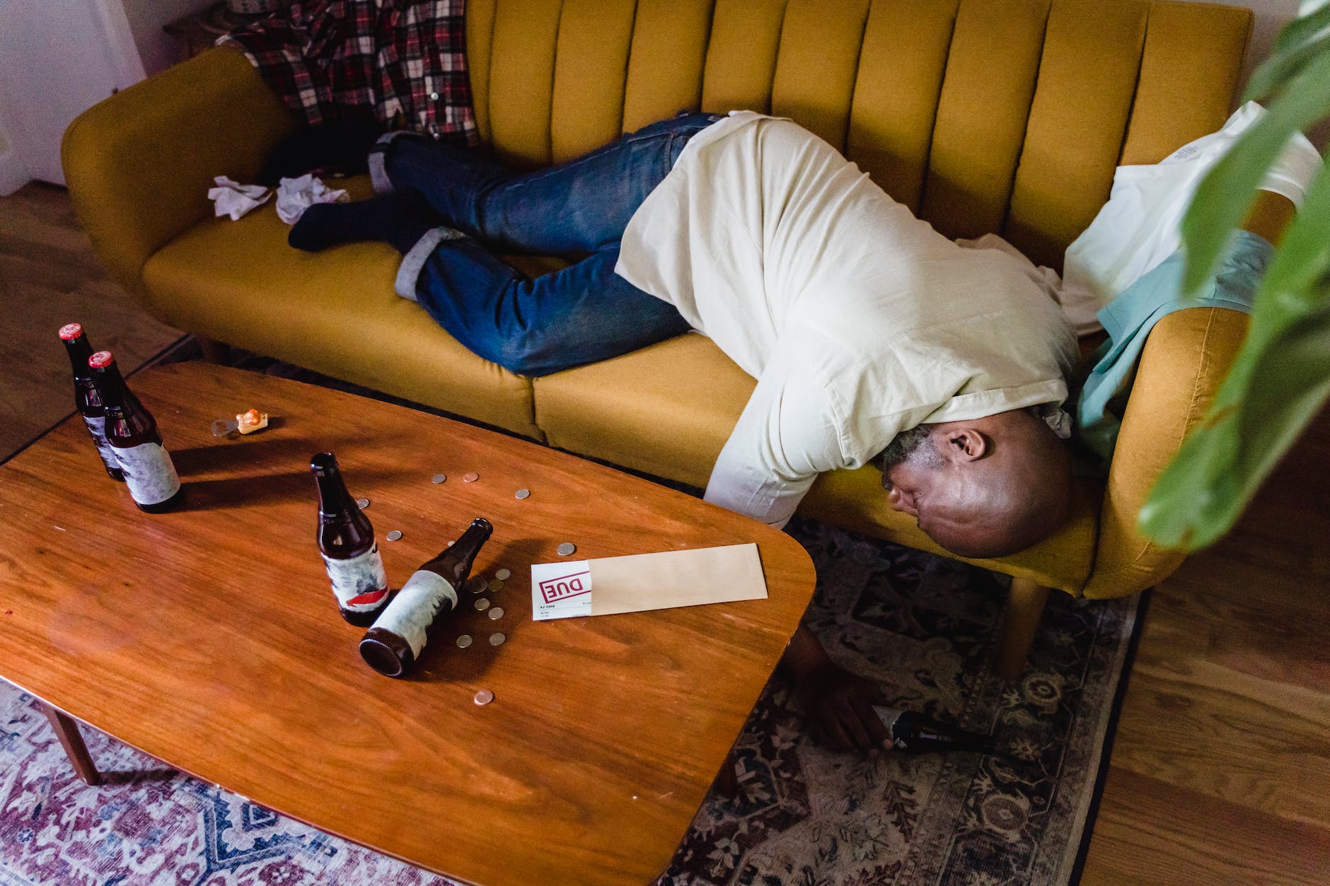 high angle view of a drunk man sleeping on a sofa and bear bottles with coins and a letter on a table